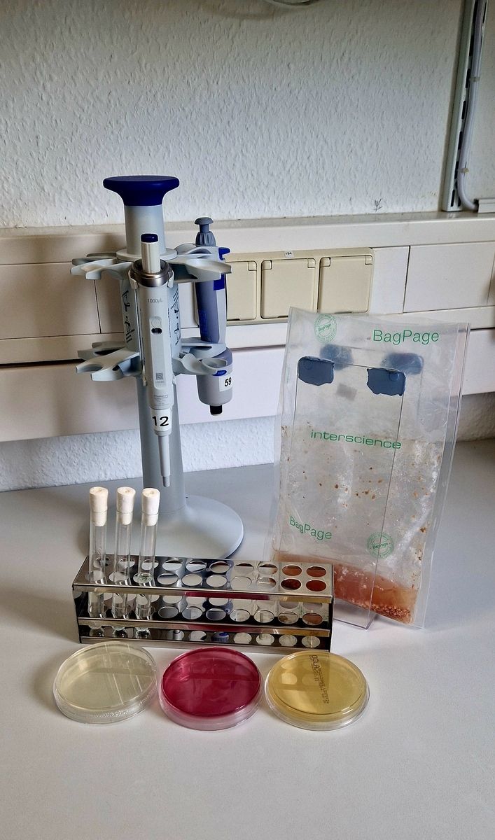 Ein Mikroskop, ein Behälter und ein Behälter mit einer Flüssigkeit auf einem Tisch angeordnet.